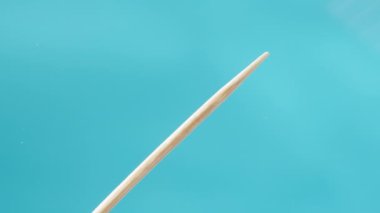 Cam Masa 'da Mavi Arkaplan' a karşı bir adamın eli tahta bir kürdanı kaldırıyor. Alt Görünüm, Yakın Çekim.