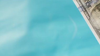 100 dolarlık banknotlar cam bir masaya fırlatılıyor, mavi bir arka plana karşı, tüm boşluğu dolduruyor. Yakın çekim, aşağıdan görünüm.