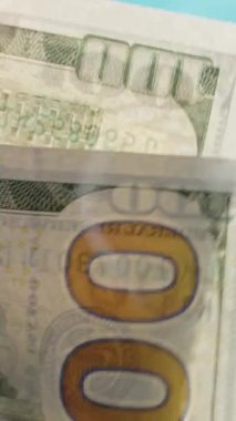 Dikey video. Bir adam mavi arka planda 100 dolarlık banknotlar sayar, aşağıdan bakar. Sonra da fırlatıyor..