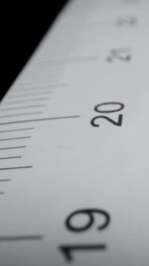 Dikey video. Siyah arka planda, santimetre ölçülü kağıt cetvel. Dolly kaydırıcı aşırı yakın çekim.