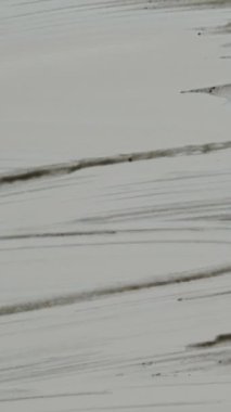 Dikey video. Camdaki toprak ya da siyah boya, adam tükürür ve siler, camın diğer tarafından aşağı bakar..