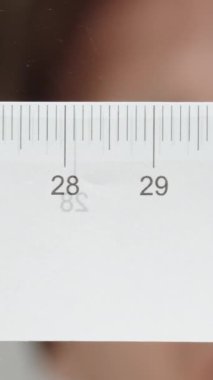 Dikey video. Camın altından bakan bir adam, cetvelle mesafeyi santimetre olarak ölçer..