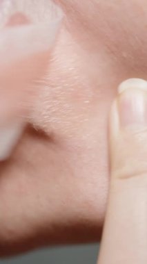 Dikey video. Bir kadın bıyık bölgesindeki kılları çıkarmak için balmumu şerit kullanır; hızla çeker, saçı yavaş çekimde, makro görünümde ayırır..