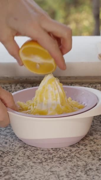 バーティカルビデオ オレンジの半分からジュースを絞る人の手 背景に果実を被る木 — ストック動画
