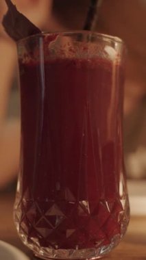 Koyu kırmızı bir kokteyli fesleğen yapraklarıyla karıştırmak, bir pipet, romantik bir akşam yemeği, arka planda bir kadınla..