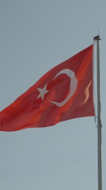 Dikey video. Mavi gökyüzüne karşı açık güneşli havada dalgalanan Türk bayrağı.