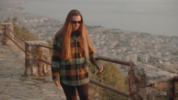 여자가 산길을 일몰에 도시와 바다와 보이는 — 비디오