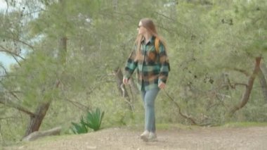 Uzun saçlı ve sıcak yeşil ekose gömlekli genç bir kadın Ormanda geziniyor, Dağ 'a doğru dik bir yolda yükseliyor..