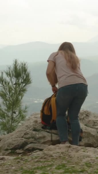 バーティカルビデオ サミットに向かう途中で岩の上に休んだ女性は 続ける準備をしている ジャーニー 頂上に独りぼっち — ストック動画