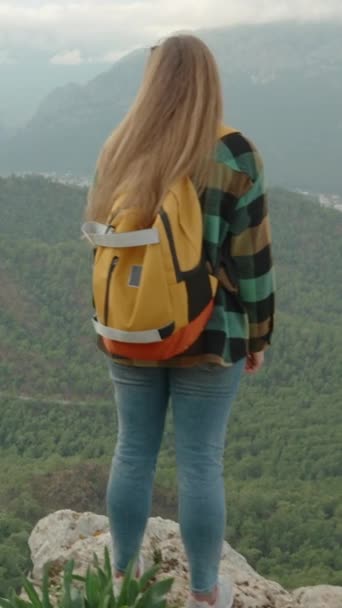 バーティカルビデオ バックパックで軽く旅する無料の若い女性 海の景色を眺めるクリフの端にあるスタンド — ストック動画
