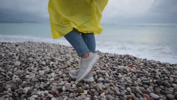 미네랄 분위기 청바지의 다리와 노란색 코트의 비치를 걸어가는 바다를 슬로우 — 비디오