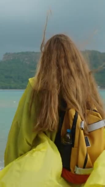 海上的风暴 天空中深蓝色的色调和蓝色的海水 一个穿着黄色雨衣背着背包的女人 她的长发被风吹乱了 — 图库视频影像