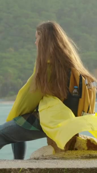 여자는 노란색 코트를 날씨에 바다에 바람에 순간을 즐긴다 — 비디오