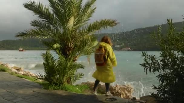 바다에서 바위에 파도가 그녀가 앞으로 이동하면서 노란색 비옷을 여자를 — 비디오