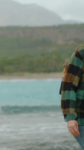 バーティカルビデオ 若くて孤独な女性旅行者 チェッカーされたシャツとバックパックのヒップスター 寒い冬の日に青いラグーン スローモーション — ストック動画
