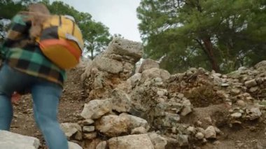 Sırt çantalı bir kadın, Phaselis şehrindeki antik bir binanın duvarlarını araştırıyor; tepeye tırmanıyor ve her köşeye bakıyor..