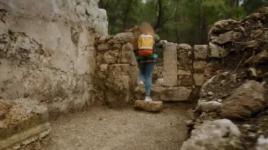 Phaselis şehrindeki eski evlerin kalıntıları, ormandaki taş duvarların kalıntıları. Sırt çantalı genç bir kadının yürüdüğü yer..