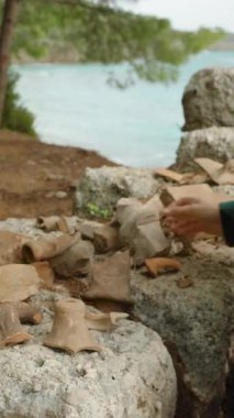 Dikey video. Deniz kenarında antik bir şehrin kazıları. Genç bir kadın kil çömlek parçalarını inceliyor..