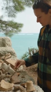 Dikey video. Deniz kıyısındaki Phaselis şehrinin kalıntılarında bulunan antik kil çömlek parçaları. Genç bir kadın onları inceliyor..