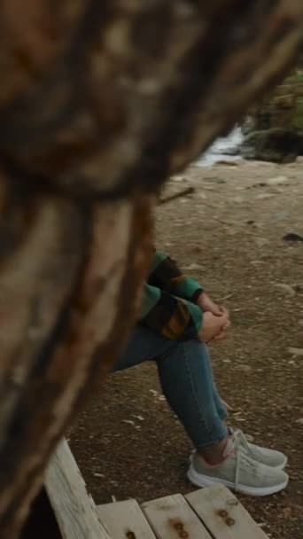 垂直录像 一位年轻女子孤零零的旅行 在海滨一棵松树下的长椅上悠闲自在地望着大海 后背一座被毁的古建筑的墙壁 — 图库视频影像