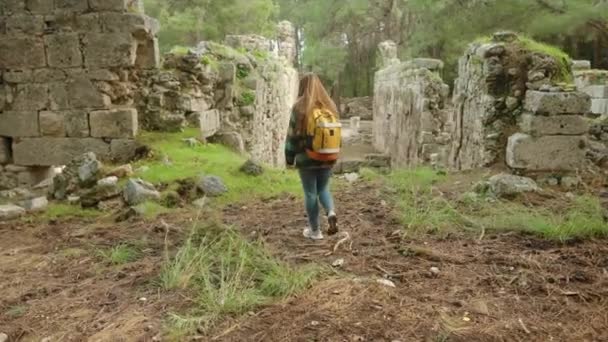 バックパック付きの女性観光客は 古代ギリシャの都市の遺跡と残骸の間で森を歩きます — ストック動画