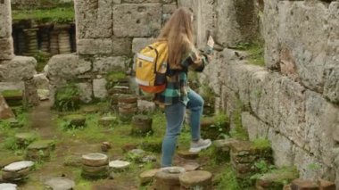 Sırt çantalı genç bir bayan gezgin antik bir Yunan şehrinin kalıntılarını araştırıyor ve sosyal medya için veya hatıra olarak fotoğraf çekiyor.