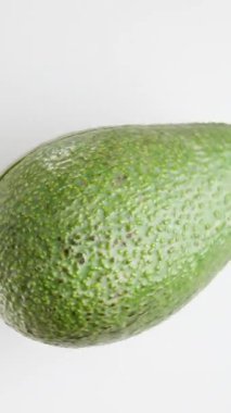 Avokado beyaz bir arkaplan üzerinde döner, hızla hızlanır ve durma noktasına geldiğinde bir çukurla bir yarıya dönüşür.