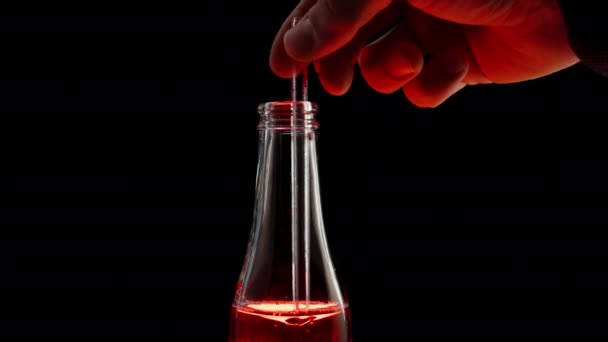 玻璃瓶中的红色苏打水用透明的吸管搅拌 在里面形成涡旋 在黑色背景下 — 图库视频影像