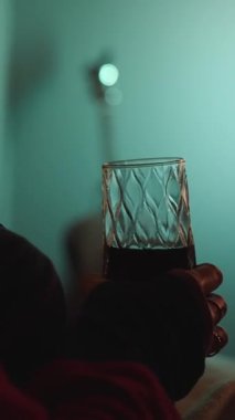 Karanlıktaki Genç Kadın TV izliyor ve bir bardaktan yudumluyor, Garland Lights 'ın arkaplanı ve TV' deki parıltısıyla.