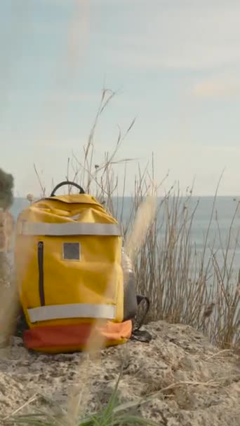Pionowe Wideo Jasnopomarańczowy Plecak Turystyczny Stoi Skraju Klifu Nad Morzem — Wideo stockowe