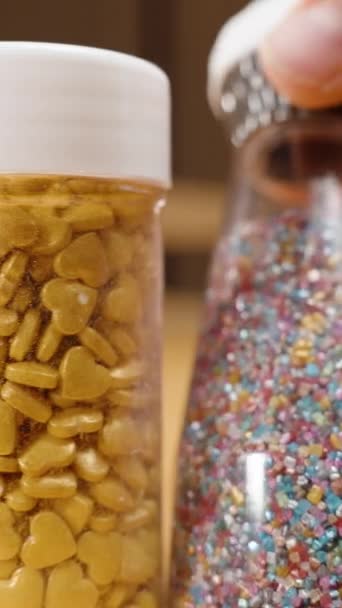 バーティカルビデオ クローズアップスライダー ペストリーを飾るために砂糖のスプラッツを選択するペストリーシェフ ハートやボールのさまざまな形や色 — ストック動画