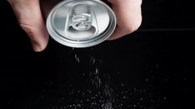 Erkek bir el siyah arka planda bir kola kutusunu tutar ve ondan şeker döker. Zararlı içecekler kavramı.