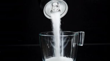 Siyah bir arka plandaki soda kutusundan şeker bir bardağa dökülüyor, izole. Zararlı içecekler. Yavaş Hareket.