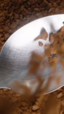 Dikey video. Çözülebilir kahve taneciklerinin arka planı kaşık içine dökülüyor, üst görünüm, yavaş çekim.