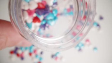 Çok renkli kalp şekerleriyle dolu bir kavanozun içinde beyaz bir arka plana döküyorum. Macro, ağır çekim..