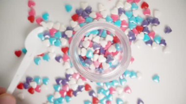 Beyaz bir masaya saçılmış çok renkli kalp şekerleri bir kavanoza konmuş. Üst görünüm, yavaş çekim.