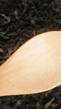 Dikey video. Kurutulmuş Büyük Çay Yaprakları Tahta Kaşık 'ın üzerine düşüyor Çay Arkaplanı, Üst Görünüm, Yavaş Hareket.