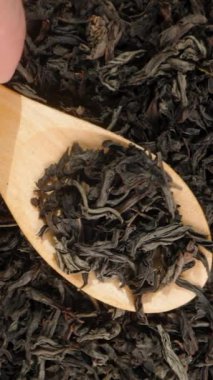 Dikey video. Kuru çay yapraklarından yapılmış bir arkaplan manzarası. Erkek El, Yapraklı Tahta Kaşık 'ı alır, Kaldırır ve Döker. Yavaş Hareket, Yakın Çekim.