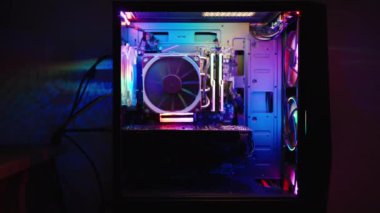 Masaüstü bilgisayarında şeffaf yan panel, pervanelerde gökkuşağı RGB aydınlatması ve içerideki elektronik bileşenler. Duvarda çok renkli yansımalar.
