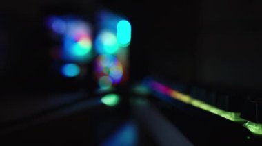 Karanlıkta gökkuşağı arka planı olan siyah klavye ve arkasında şeffaf bir kapağı olan oyun bilgisayarı ve RGB ışıklı hayranlar..