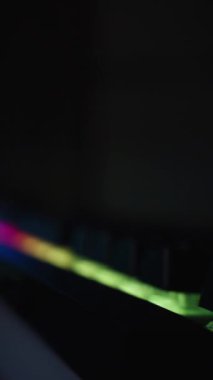 Dikey video. Karanlıkta gökkuşağı arka planı olan siyah klavye ve arkasında şeffaf bir kapağı olan oyun bilgisayarı ve RGB ışıklı hayranlar..