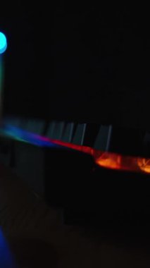 Dikey video. Masaüstü oyun bilgisayarı, gökkuşağı renkleriyle parlayan karanlık bir odada, kamera odağı masadaki klavyeden arka plana kayıyor..