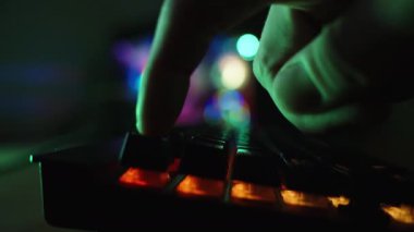 Oyun bilgisayarından gökkuşağı aydınlatmalı karanlık oda, bir parmağın tuşa bastığı bir klavye, yakın plan..