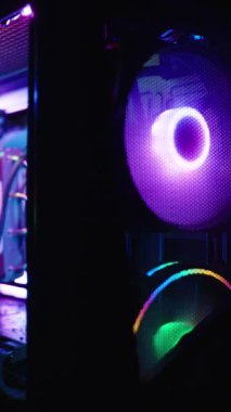 Dikey video. Saydam yan paneli olan bir oyun bilgisayarı olan karanlık oda RGB ışıklandırmalı dahili bileşenleri ve uzaktaki bir monitörü gösteriyor..