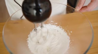 Tahta bir masada, bir pasta şefi beyaz kremayı elektrikli mikserle karıştırmak için çırpar..