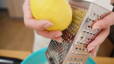 Bir kadın metal rendeleyicisinde limon rendeliyor, yavaş çekimde yakın plan..