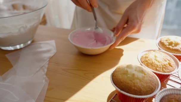 ペストリーシェフは 日光に照らされたカップケーキを飾るためにピンクのフロスティングをかき混ぜます スローモーション — ストック動画