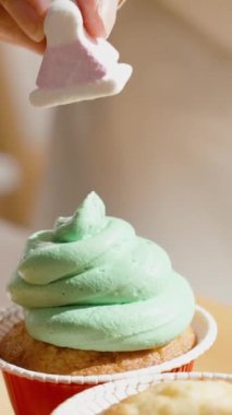 Bir kadın çöreği yeşil kremanın üzerinde noel ağacı şeklinde bir şekerle süslüyor..