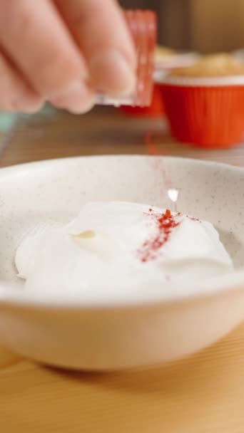 ペストリーシェフは白いカップケーキのフロスティングに赤い染料をポーズします — ストック動画