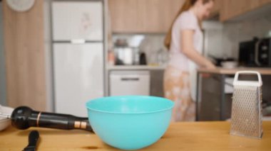 Parlak bir mutfakta, arka planda ahşap bir iç mekanı olan, odaktan uzak, mutfak aletleriyle dolu bir masa olan bir kadın..